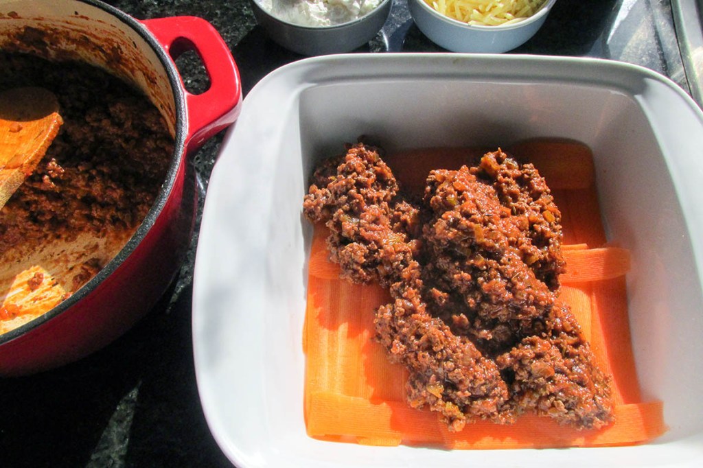Next add a half of the meat and sauce to create a layer in the baking dish.